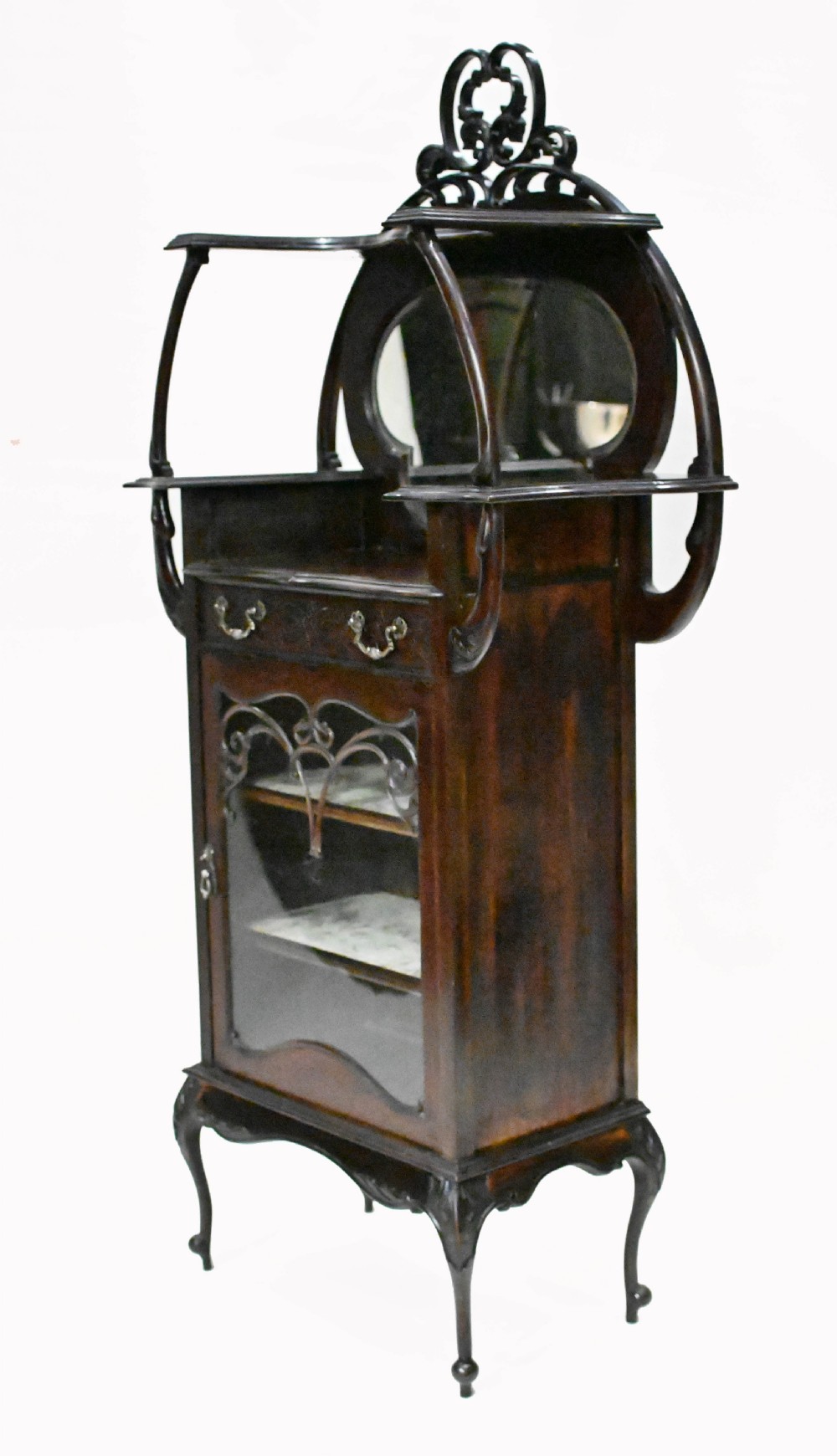 A dark mahogany Art Nouveau display cabinet featuring a pierced cresting, an asymmetrical mirrored superstructure, a single drawer, and a glazed door on slender shaped legs. View IV