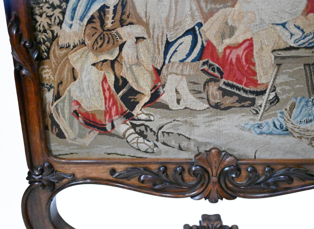 An early Victorian carved wooden fire screen featuring a hand-worked needlepoint tapestry of a pastoral scene set within a scrolled frame. View V