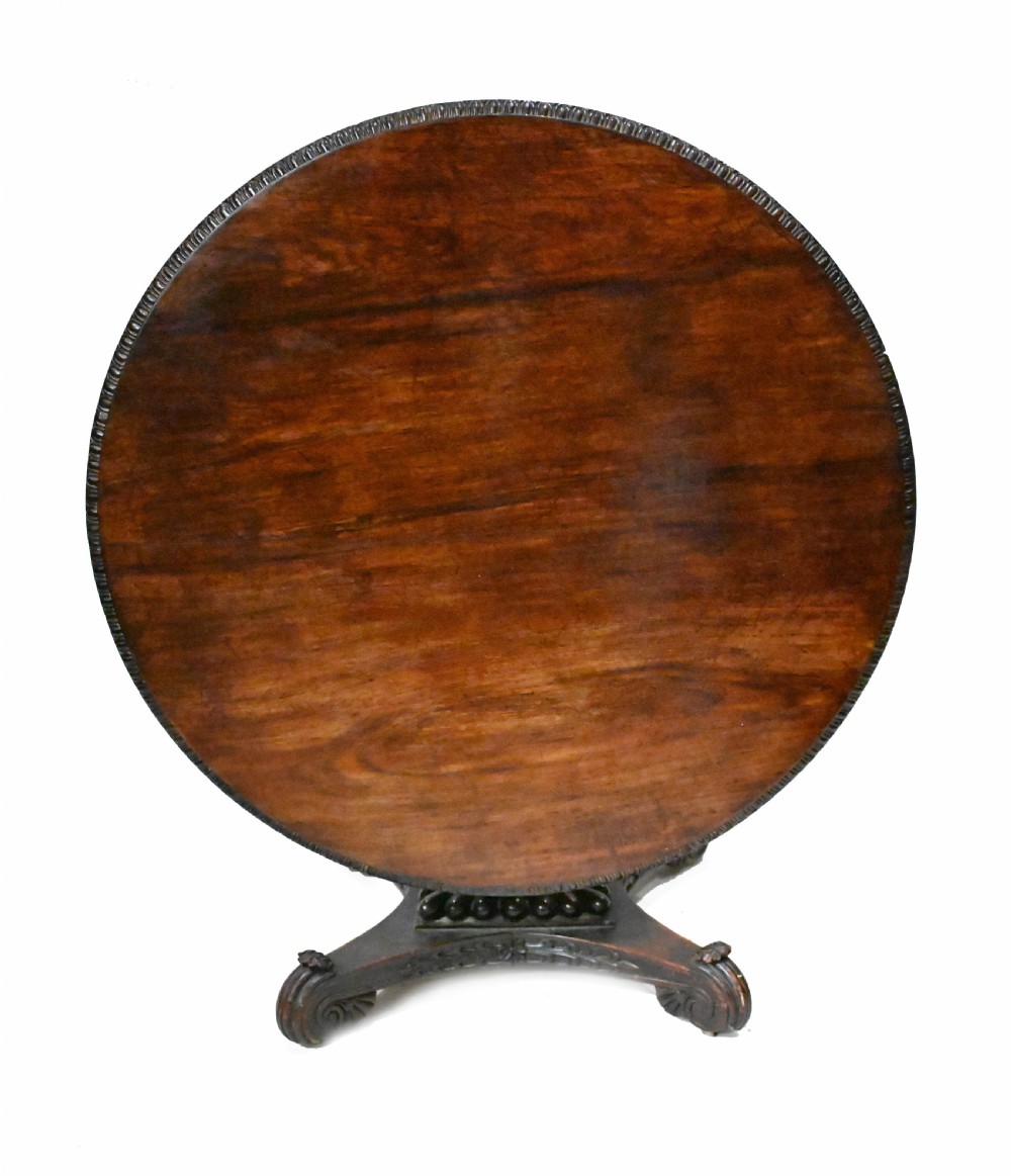 An 1840s Anglo-Indian tilt-top centre table featuring a circular padauk wood top set upon a carved pedestal base.