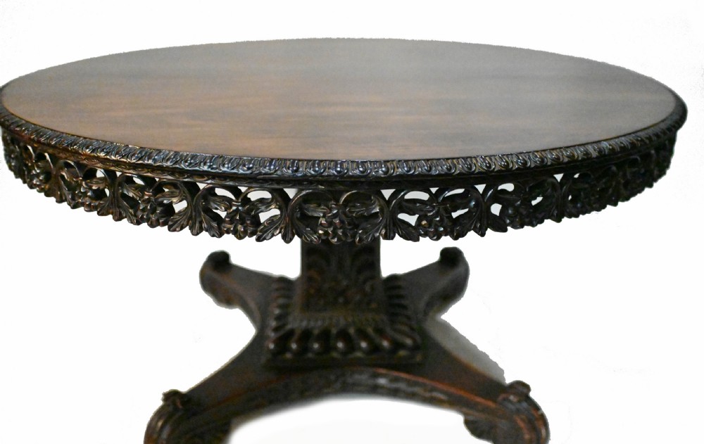 An 1840s Anglo-Indian tilt-top centre table featuring a circular padauk wood top set upon a carved pedestal base. View V