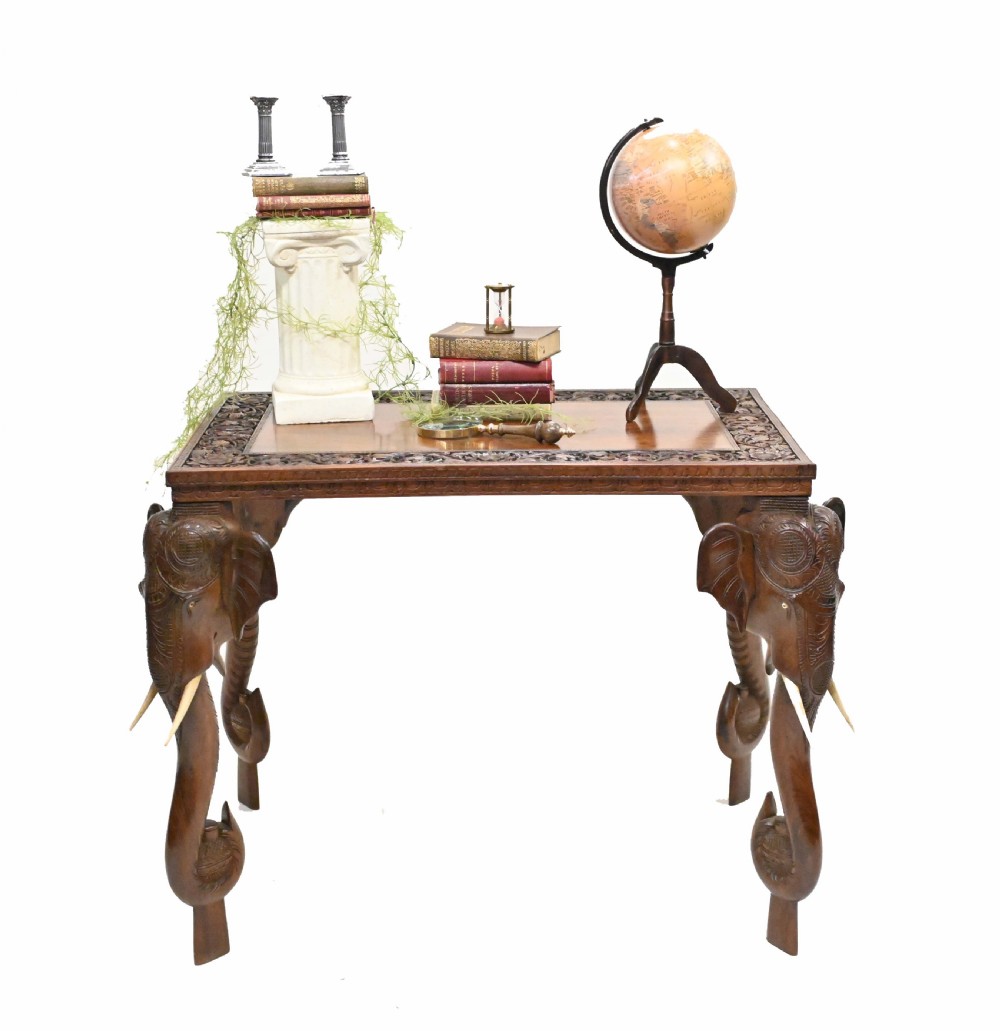 A dark timber rectangular side table featuring a carved foliage border and four legs sculpted as elephant heads with trunks extending to the floor. View VII
