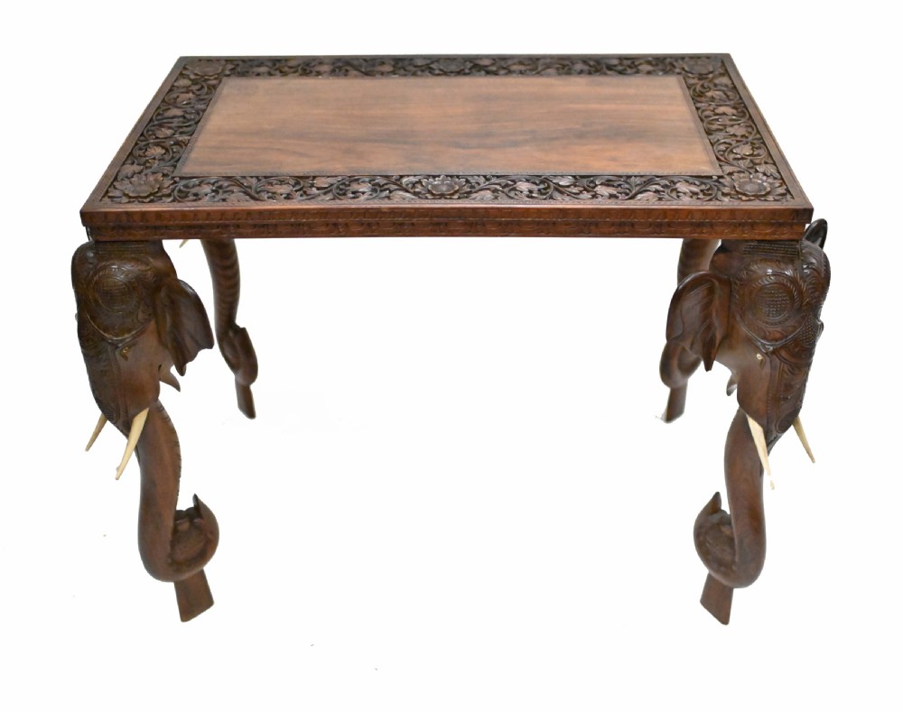 A dark timber rectangular side table featuring a carved foliage border and four legs sculpted as elephant heads with trunks extending to the floor.