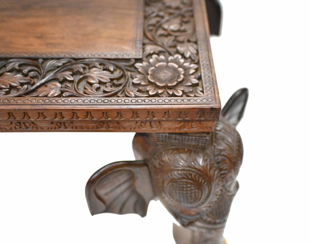 A dark timber rectangular side table featuring a carved foliage border and four legs sculpted as elephant heads with trunks extending to the floor. View X