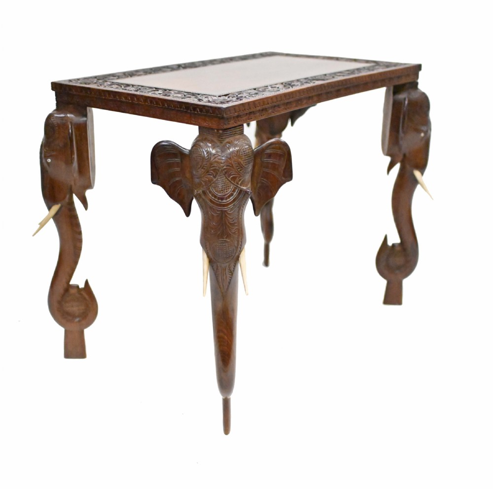 A dark timber rectangular side table featuring a carved foliage border and four legs sculpted as elephant heads with trunks extending to the floor. View XII