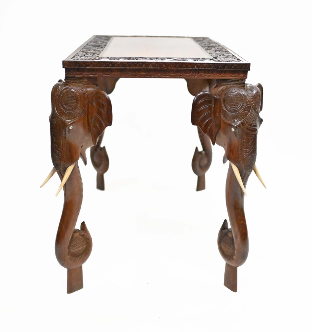A dark timber rectangular side table featuring a carved foliage border and four legs sculpted as elephant heads with trunks extending to the floor. View XIV