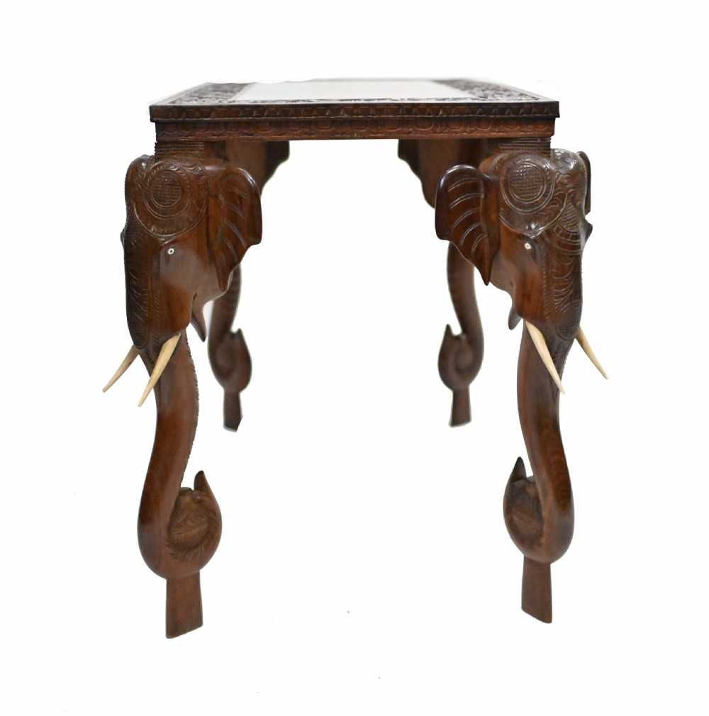 A dark timber rectangular side table featuring a carved foliage border and four legs sculpted as elephant heads with trunks extending to the floor. View XV