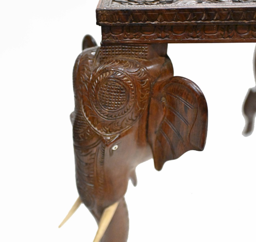 A dark timber rectangular side table featuring a carved foliage border and four legs sculpted as elephant heads with trunks extending to the floor. View XVII
