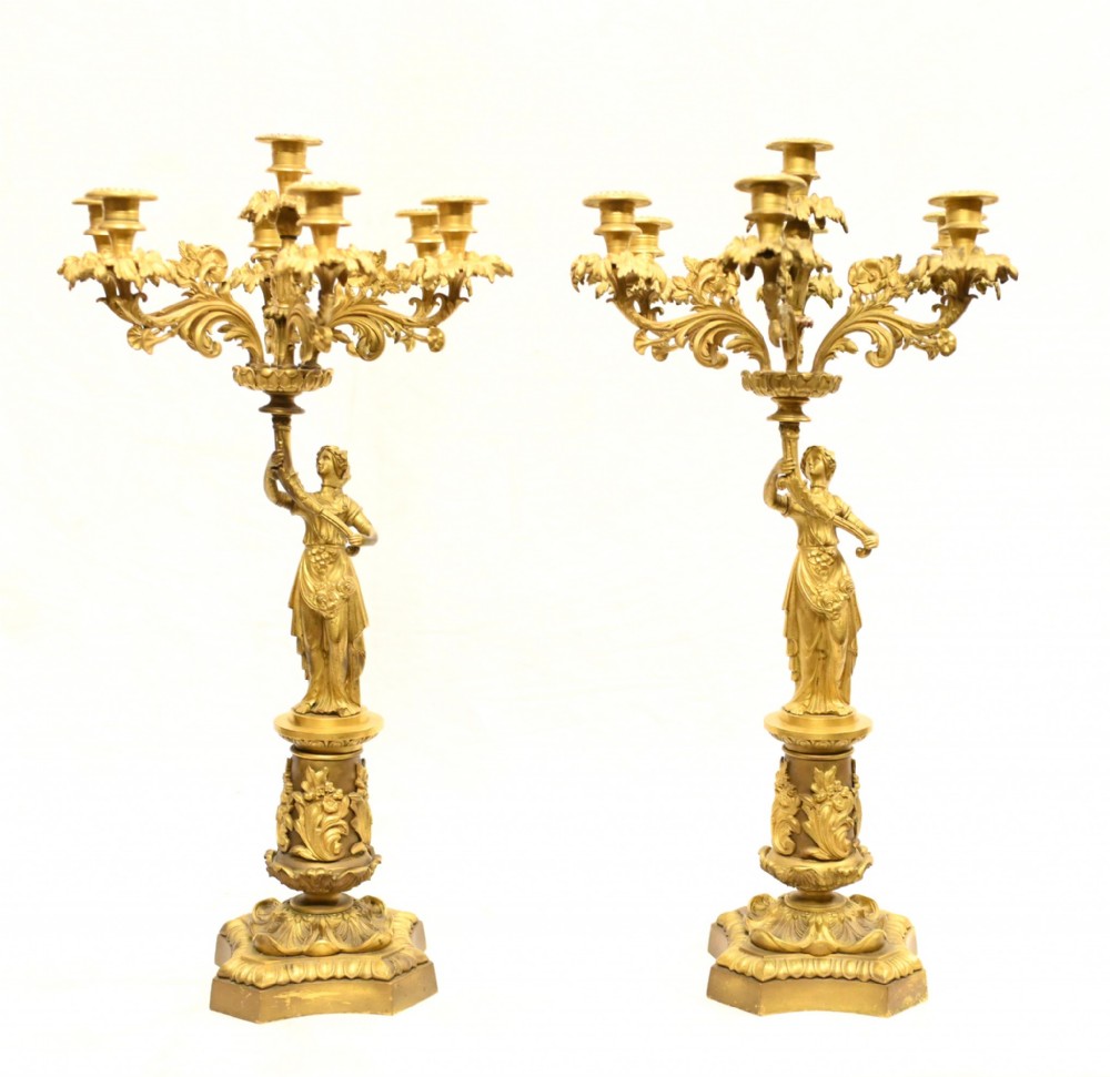 A pair of nineteenth-century French ormolu gilt bronze candelabras featuring classical maiden figures supporting six scrolling leafy candle branches on decorative plinths.