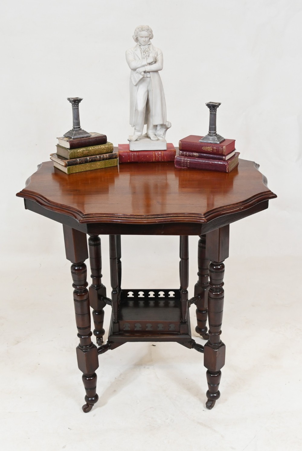 A late Victorian dark mahogany parlour table with a shaped octagonal top, turned legs on castors, and a lower shelf featuring a pierced gallery.