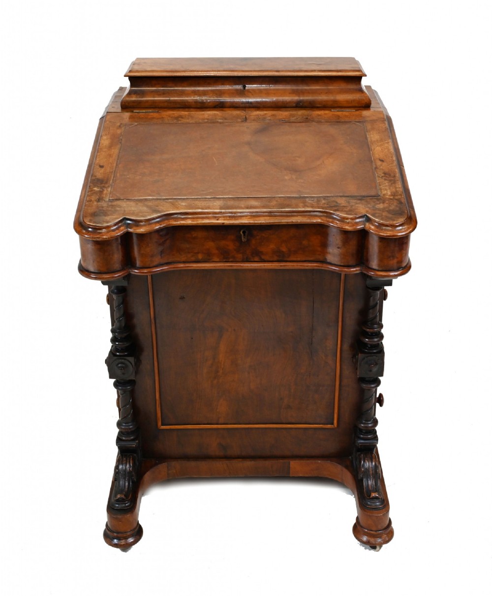A Victorian walnut Davenport desk featuring a sloping leather writing surface, a raised top compartment, and carved column supports.
