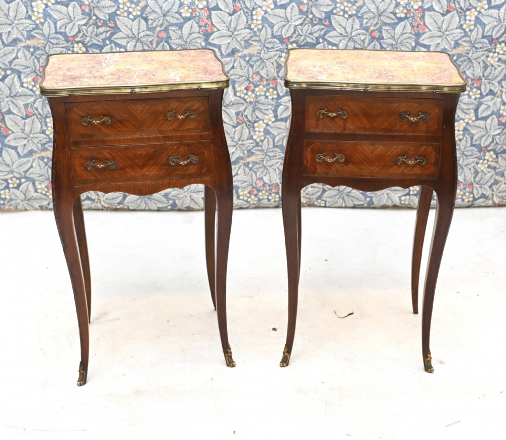 A pair of French Louis XV style wooden bedside tables featuring two drawers with brass handles, cabriole legs with brass feet, and mottled pink marble tops.