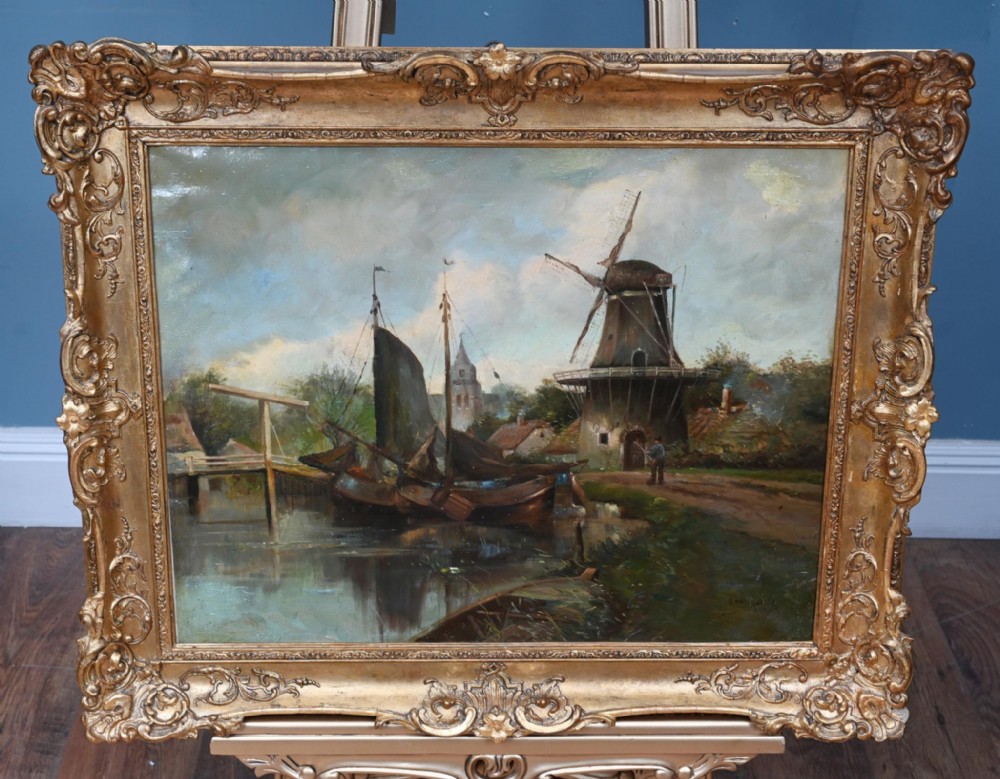 An oil painting depicting a Dutch canal scene with a windmill and sailboat, enclosed within an ornate giltwood frame.