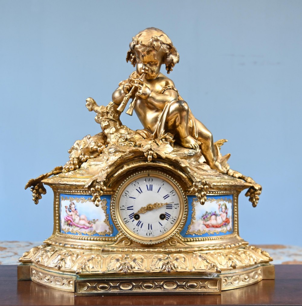 A late 19th-century French Rococo gilt bronze mantel clock featuring a sculpted cherub playing a pipe atop, flanked by sky-blue painted porcelain plaques.