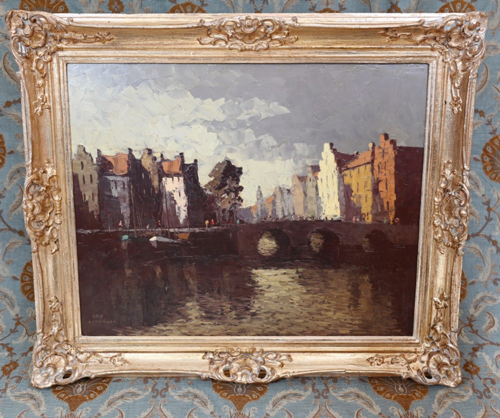 An expressionist oil painting depicting a canal with buildings and a stone bridge, enclosed within an ornate gilded frame.