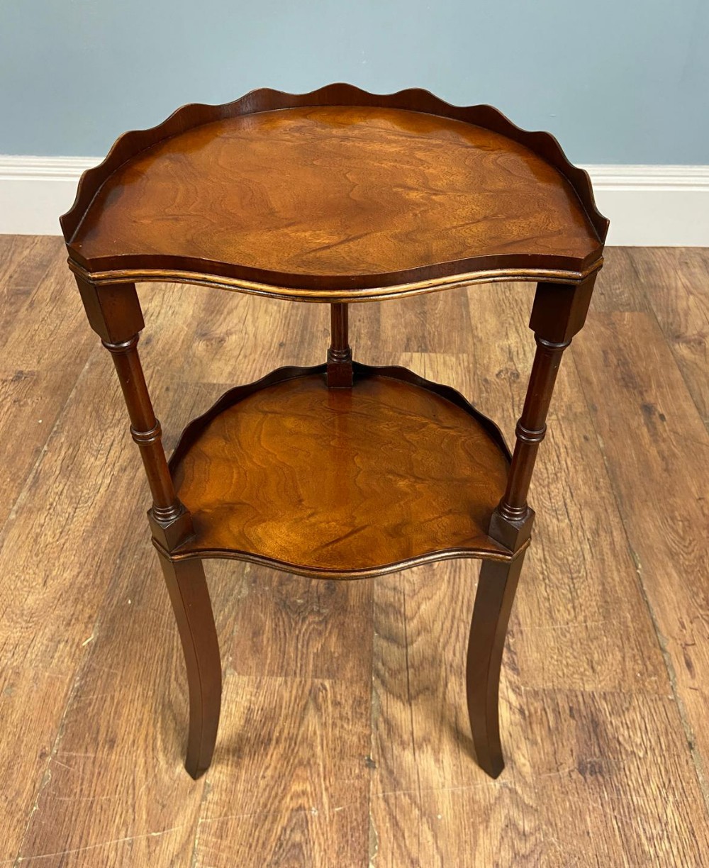 An Edwardian walnut two-tier side table featuring a scalloped top rim, turned upper leg supports, and curved lower legs.