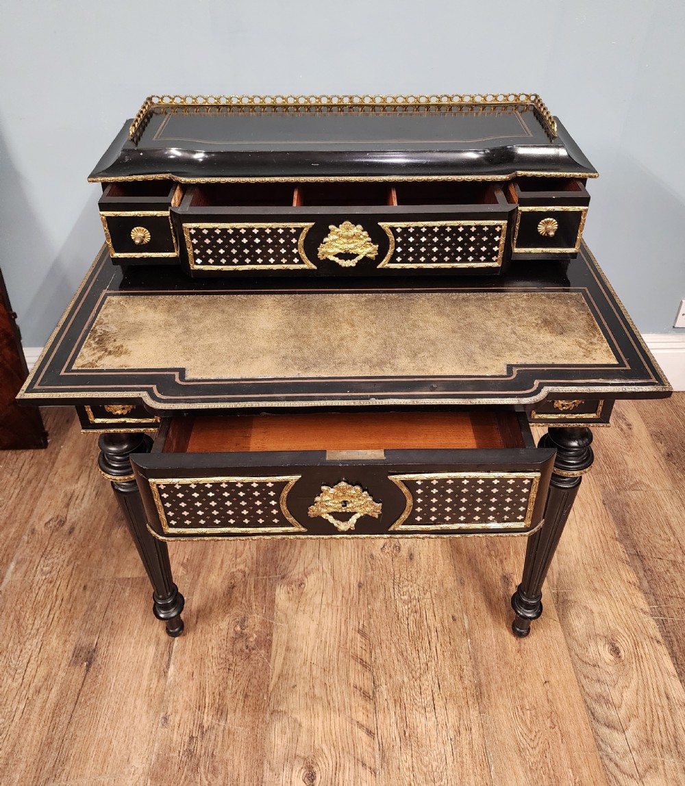 A French Napoleon III ebonised writing desk featuring gilt bronze mounts, brass inlay panels, turned legs, and a raised top superstructure with a brass gallery. View VII