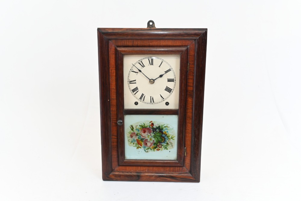 A rectangular dark wood framed American wall clock featuring a white dial with Roman numerals above a painted floral lower glass panel.