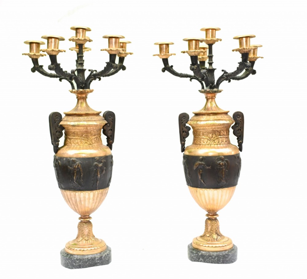 A symmetrical pair of antique gilt and dark patinated bronze multi-branch candelabras shaped like Classical urns on grey marble bases.