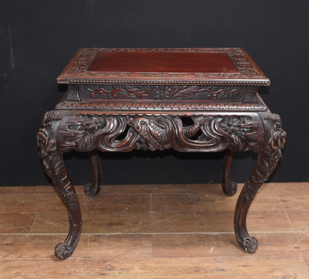 An antique dark brown hardwood side table featuring deep relief carvings of foliage and aquatic motifs along the apron and legs.