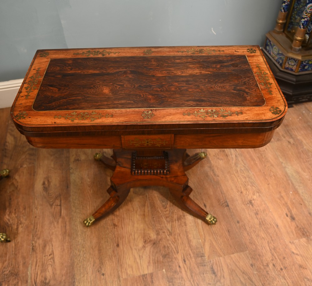 A pair of Regency rosewood and mahogany fold-over card tables featuring brass foliate inlay, central pedestal stems, and splayed quadform legs with brass paw castors. View II
