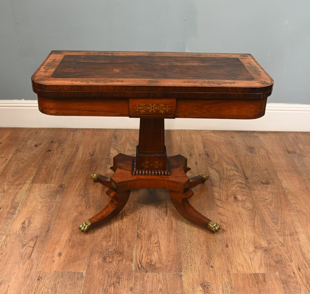 A pair of Regency rosewood and mahogany fold-over card tables featuring brass foliate inlay, central pedestal stems, and splayed quadform legs with brass paw castors. View III