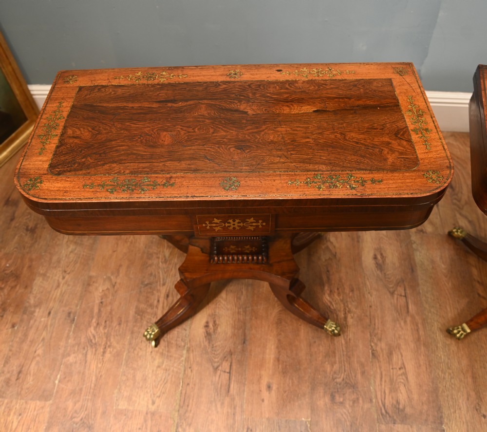 A pair of Regency rosewood and mahogany fold-over card tables featuring brass foliate inlay, central pedestal stems, and splayed quadform legs with brass paw castors. View IV