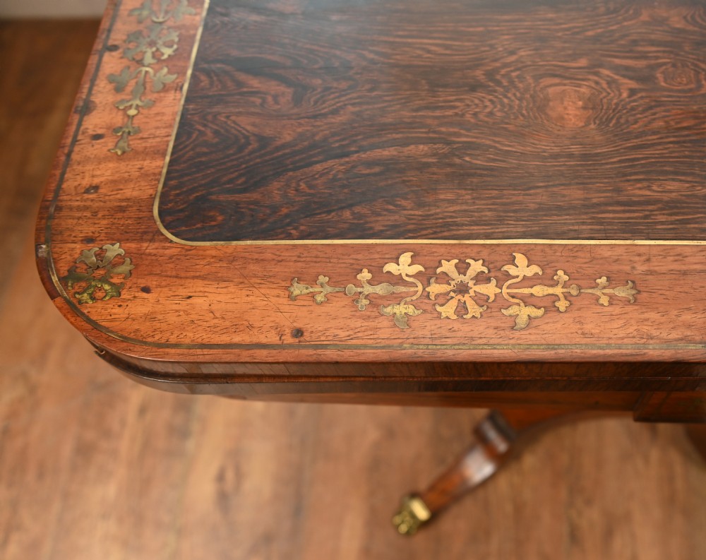 A pair of Regency rosewood and mahogany fold-over card tables featuring brass foliate inlay, central pedestal stems, and splayed quadform legs with brass paw castors. View V