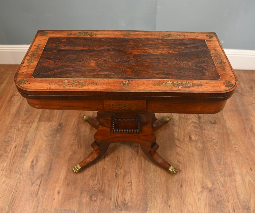 A pair of Regency rosewood and mahogany fold-over card tables featuring brass foliate inlay, central pedestal stems, and splayed quadform legs with brass paw castors. View VI
