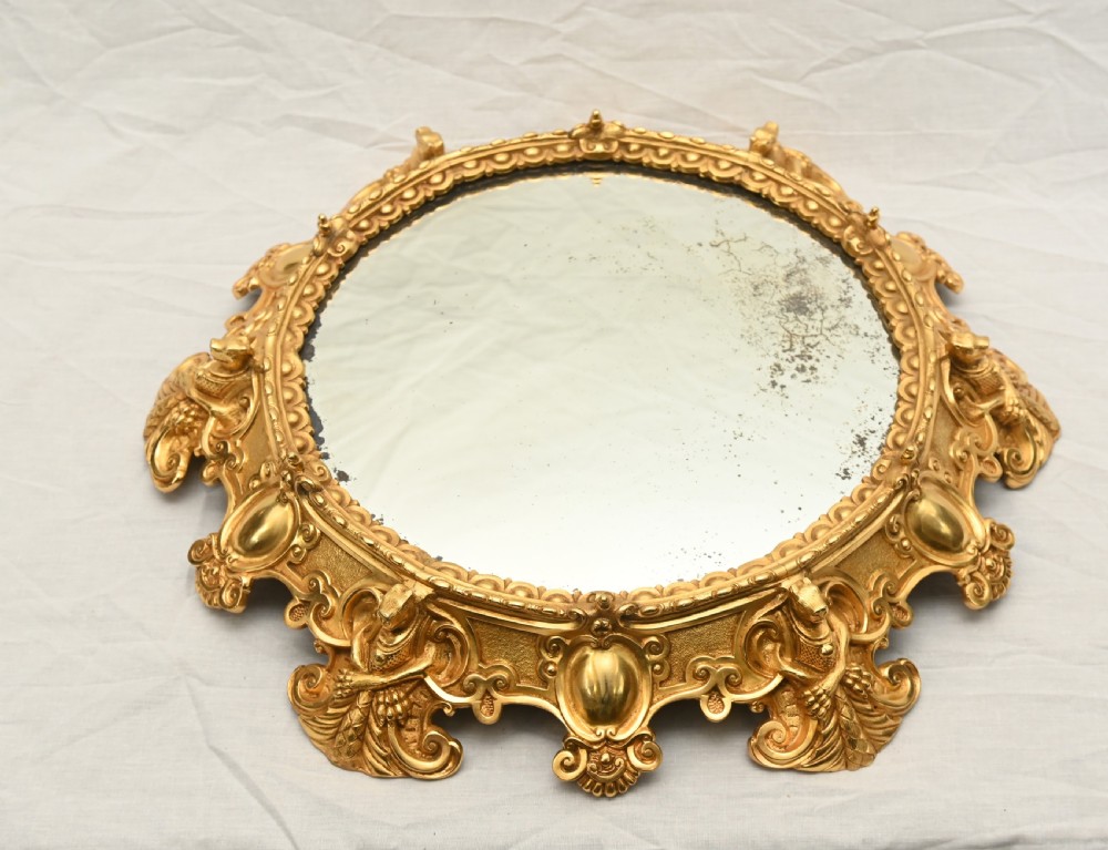 A circular French Rococo style gilt bronze mirrored plateau featuring an ornate scrollwork frame with decorative feet and a foxed mirror insert. View IV