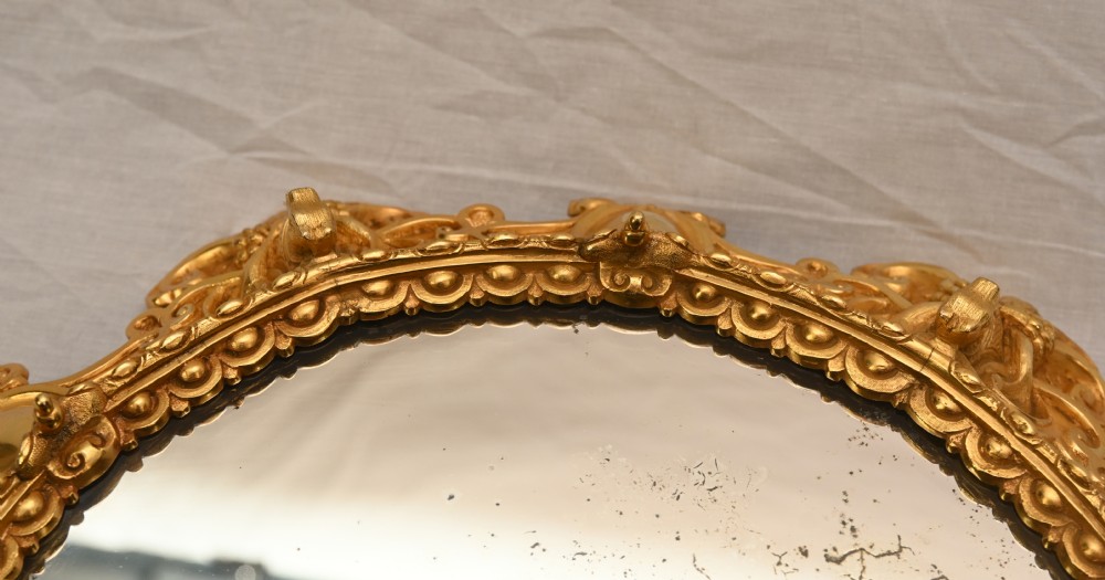 A circular French Rococo style gilt bronze mirrored plateau featuring an ornate scrollwork frame with decorative feet and a foxed mirror insert. View V