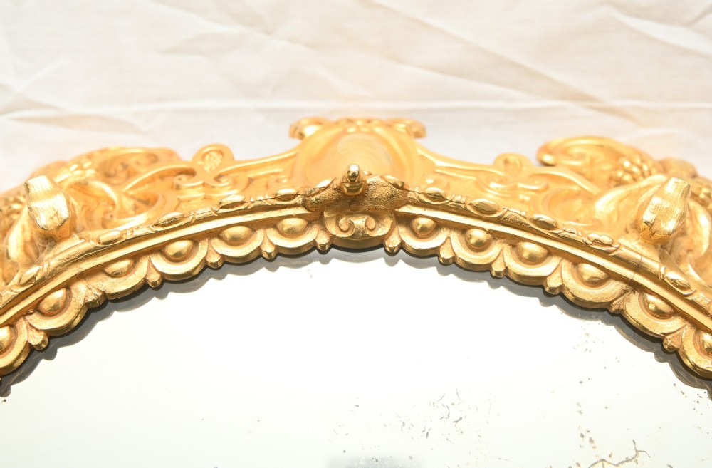 A circular French Rococo style gilt bronze mirrored plateau featuring an ornate scrollwork frame with decorative feet and a foxed mirror insert. View VI