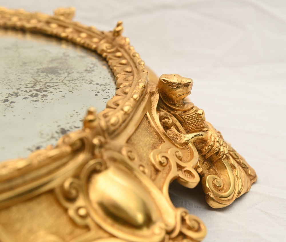 A circular French Rococo style gilt bronze mirrored plateau featuring an ornate scrollwork frame with decorative feet and a foxed mirror insert. View VII