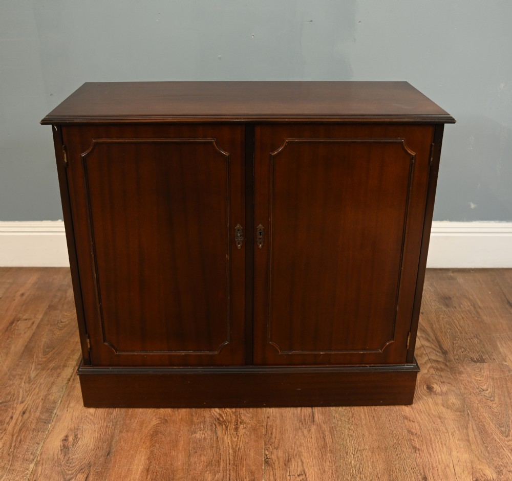 An early Victorian dark mahogany side cabinet featuring two panelled cupboard doors with brass keyhole escutcheons and a plinth base.