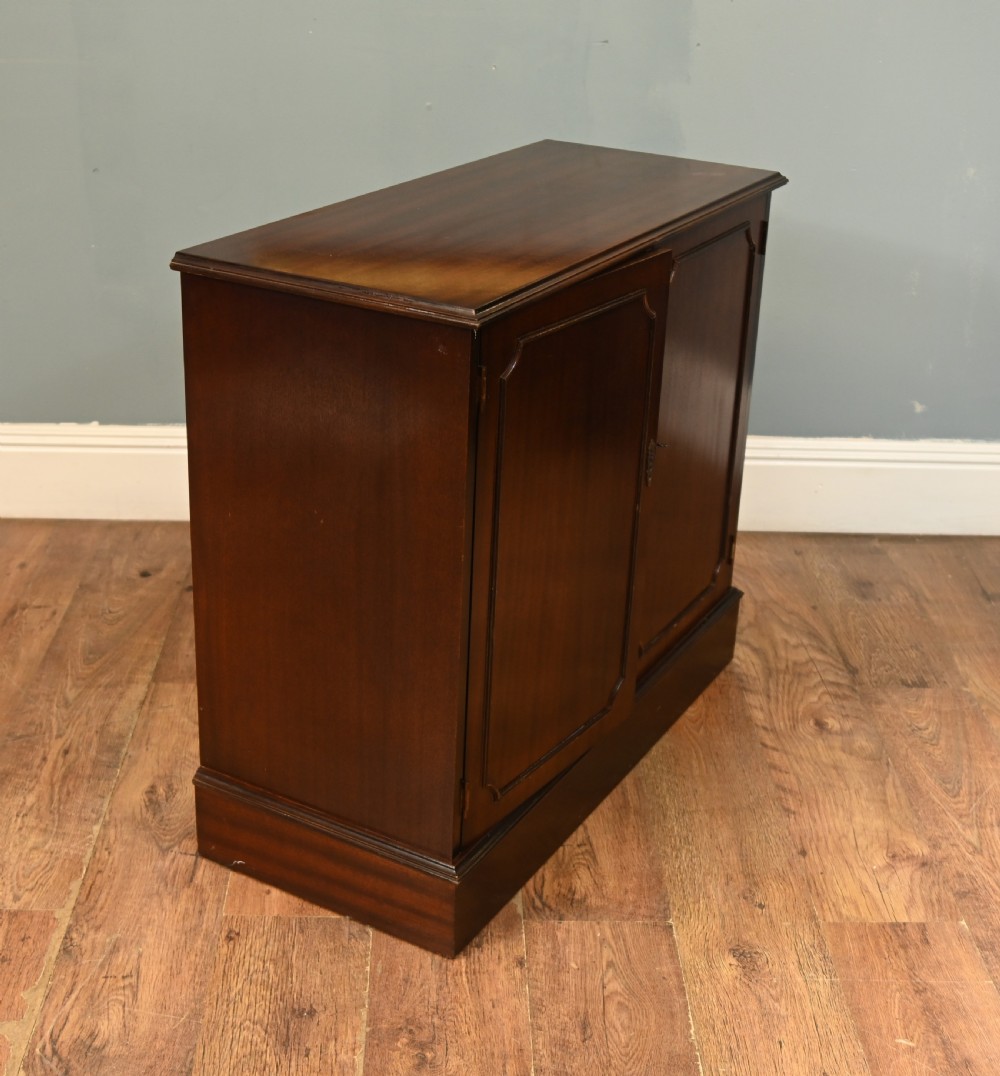 An early Victorian dark mahogany side cabinet featuring two panelled cupboard doors with brass keyhole escutcheons and a plinth base. View IV
