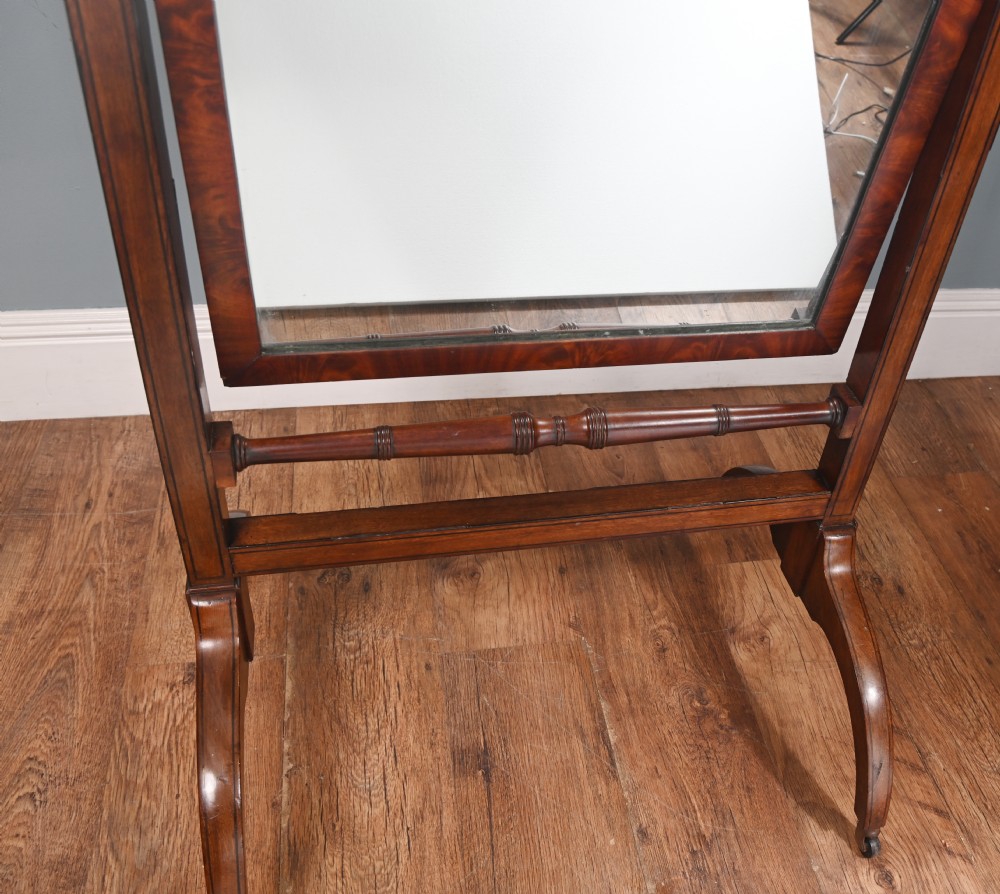 A Regency mahogany cheval mirror featuring an adjustable rectangular mirror plate, turned urn finials, a turned stretcher, and splayed legs on brass castors. View IV