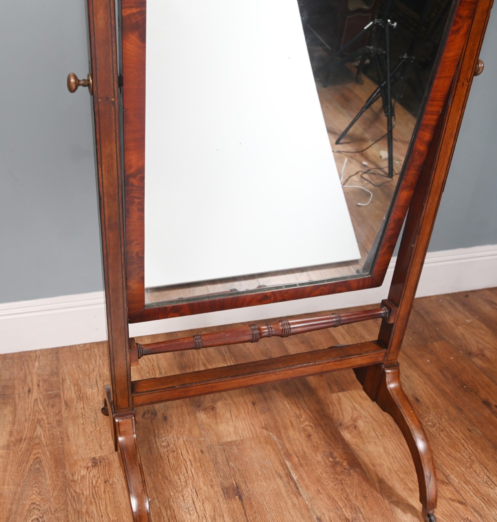 A Regency mahogany cheval mirror featuring an adjustable rectangular mirror plate, turned urn finials, a turned stretcher, and splayed legs on brass castors. View V