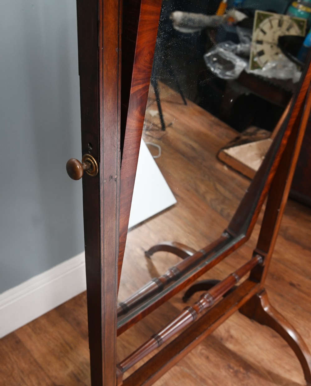 A Regency mahogany cheval mirror featuring an adjustable rectangular mirror plate, turned urn finials, a turned stretcher, and splayed legs on brass castors. View VI