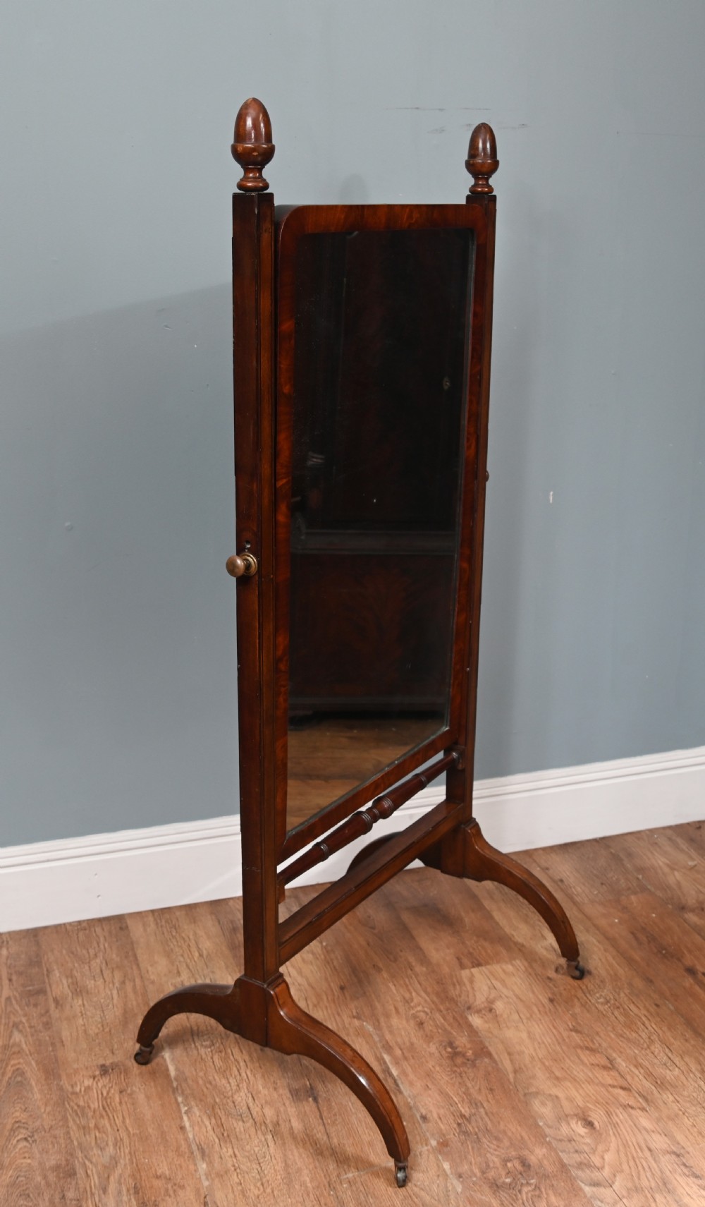 A Regency mahogany cheval mirror featuring an adjustable rectangular mirror plate, turned urn finials, a turned stretcher, and splayed legs on brass castors. View VII