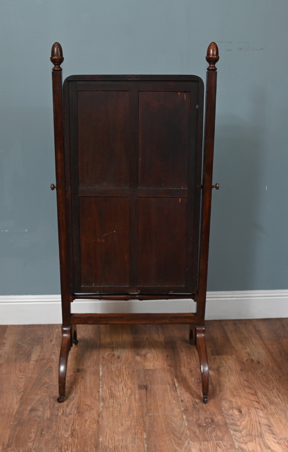 A Regency mahogany cheval mirror featuring an adjustable rectangular mirror plate, turned urn finials, a turned stretcher, and splayed legs on brass castors. View XI