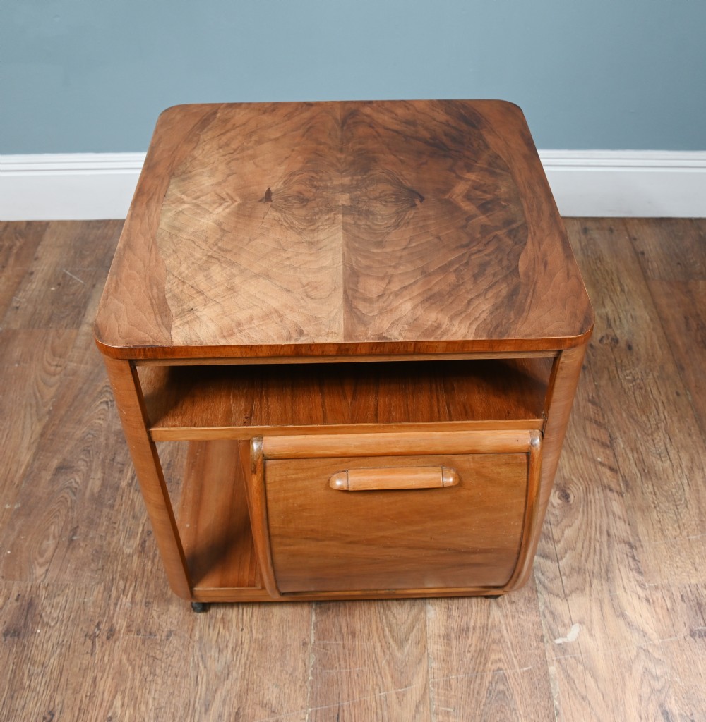 An Art Deco walnut side table featuring a square top, open shelving, a central drop-front cabinet compartment, and small base castors. View III