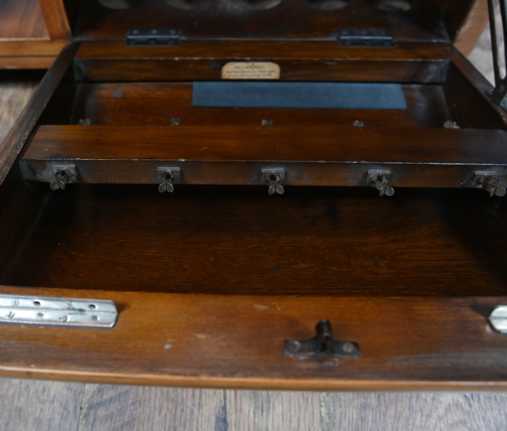 An Art Deco walnut side table featuring a square top, open shelving, a central drop-front cabinet compartment, and small base castors. View VI