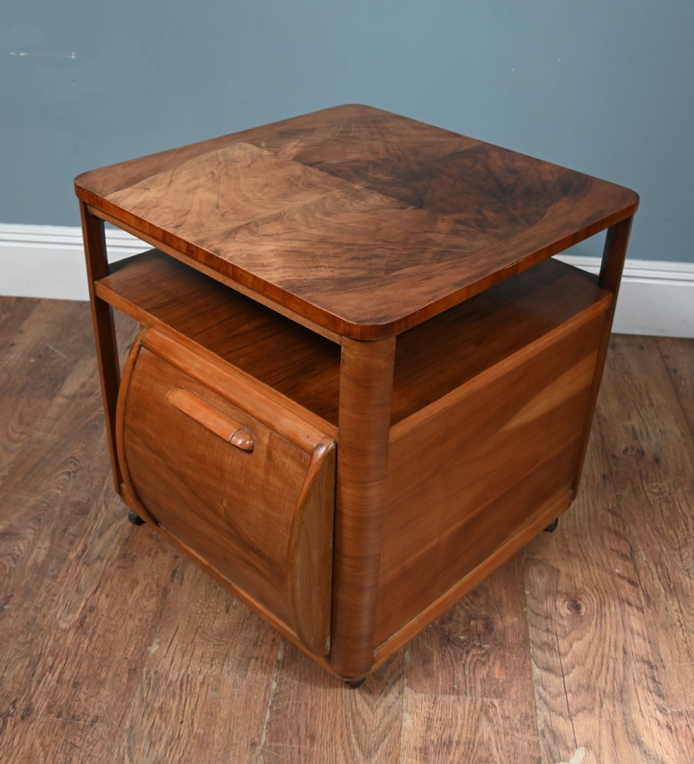 An Art Deco walnut side table featuring a square top, open shelving, a central drop-front cabinet compartment, and small base castors. View VII