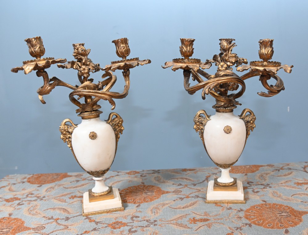 A pair of late 19th-century French Louis XVI Revival gilt bronze and white marble three-arm candelabras featuring urn-shaped bases and floral branch detailing.