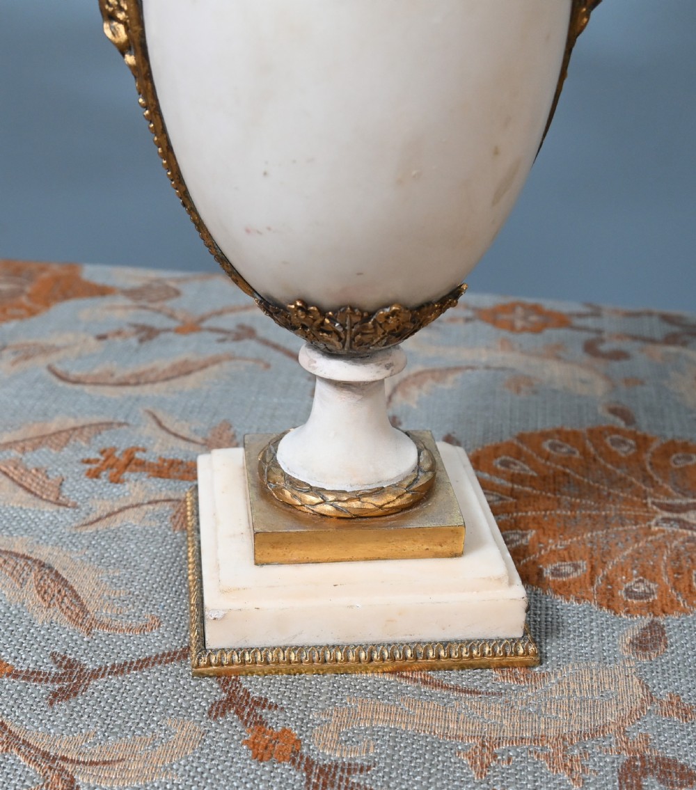A pair of late 19th-century French Louis XVI Revival gilt bronze and white marble three-arm candelabras featuring urn-shaped bases and floral branch detailing. View IV