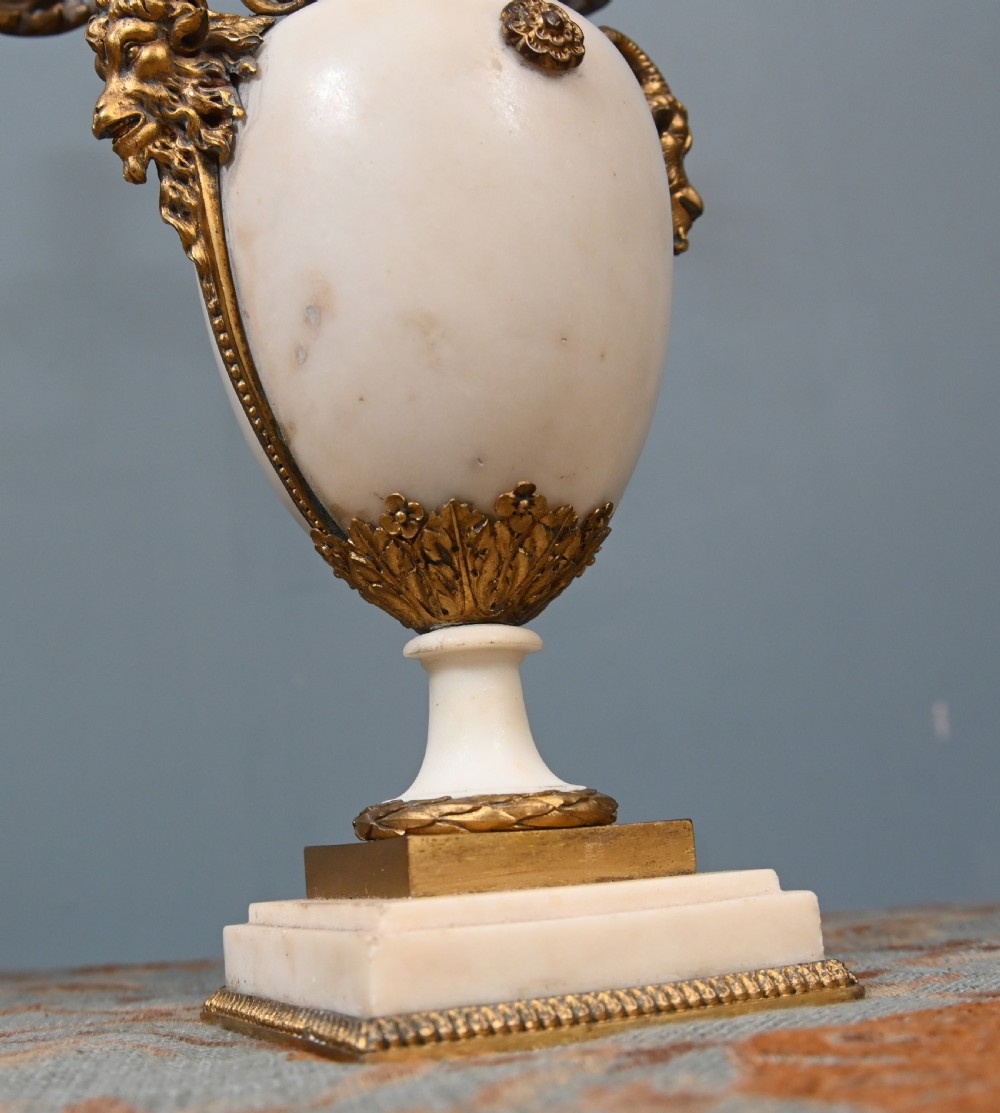 A pair of late 19th-century French Louis XVI Revival gilt bronze and white marble three-arm candelabras featuring urn-shaped bases and floral branch detailing. View XVI