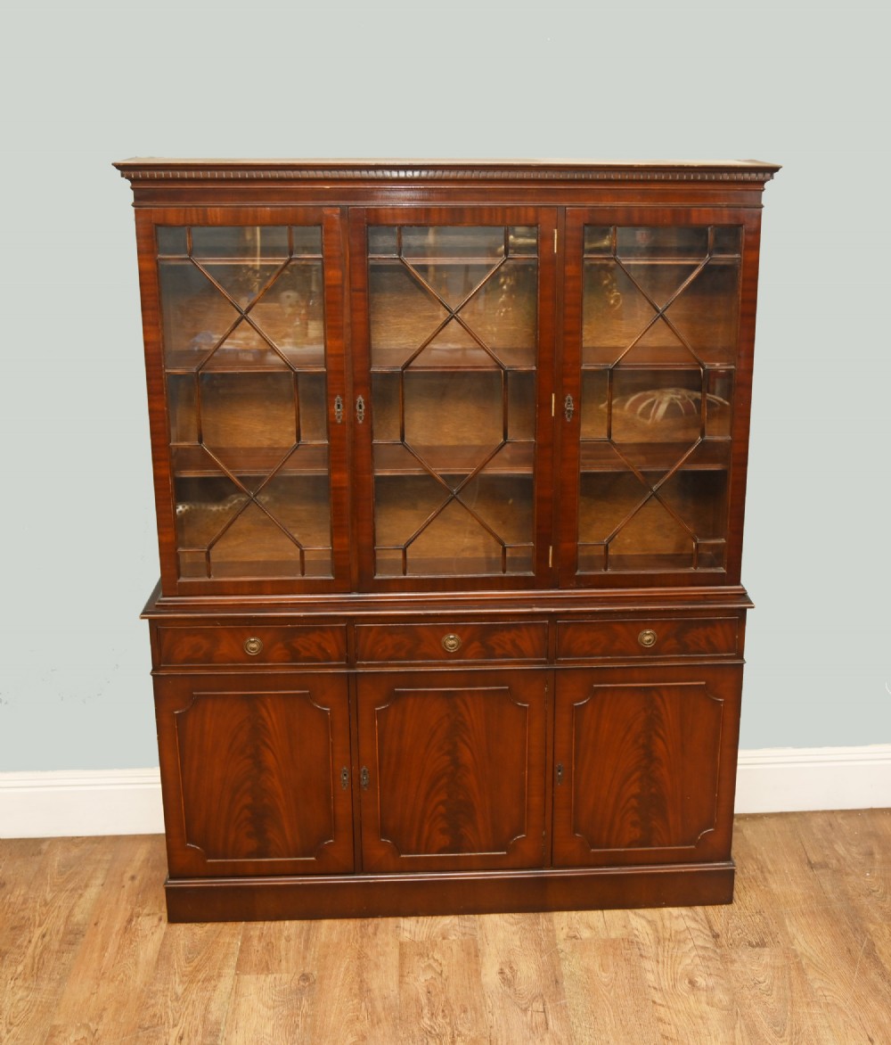A Georgian Revival mahogany bookcase cabinet featuring a three-door astragal glazed upper section above three drawers and flame mahogany cupboard doors.