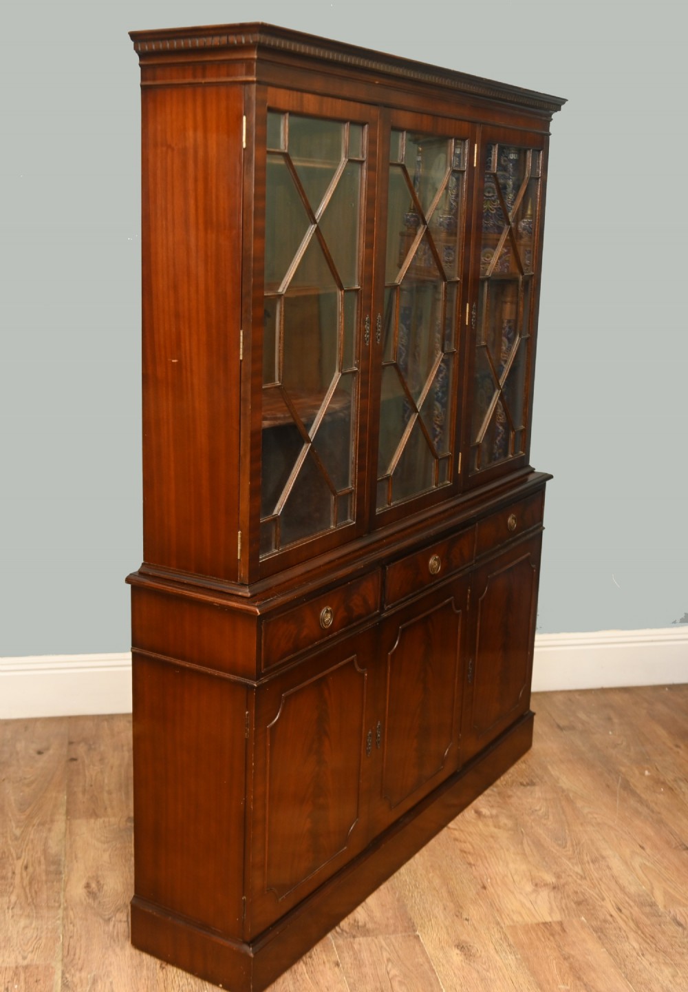 A Georgian Revival mahogany bookcase cabinet featuring a three-door astragal glazed upper section above three drawers and flame mahogany cupboard doors. View X