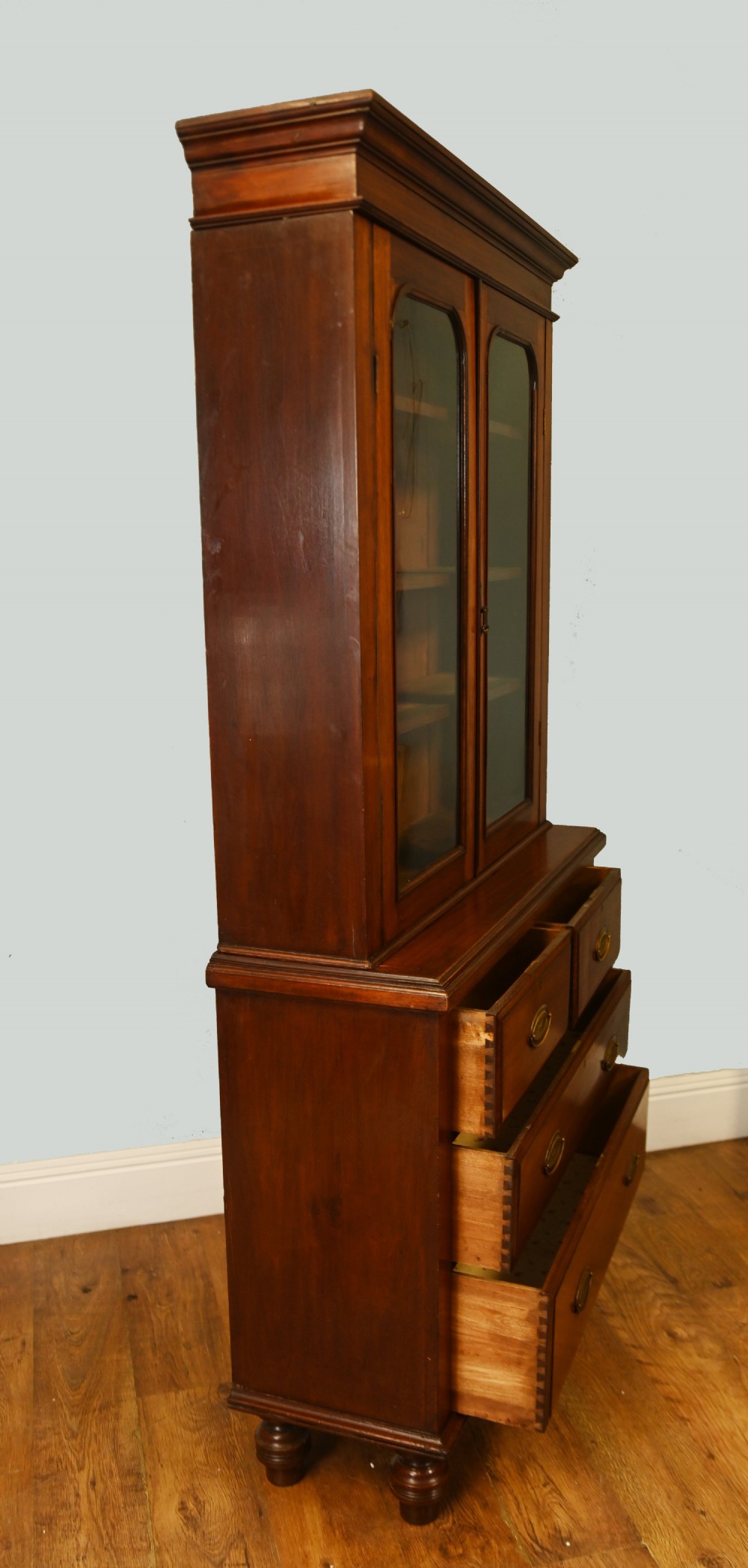 Victorian mahogany glazed bookcase featuring a two-door glass cabinet section resting on a chest of four drawers with brass handles. View VII