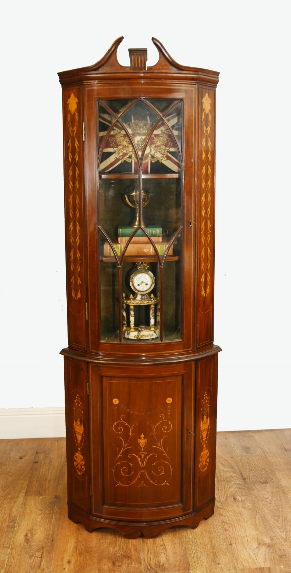 An Edwardian inlaid mahogany corner display cabinet featuring a swan-neck pediment, astragal glazed upper door, and marquetry urn designs on the lower panel. View II