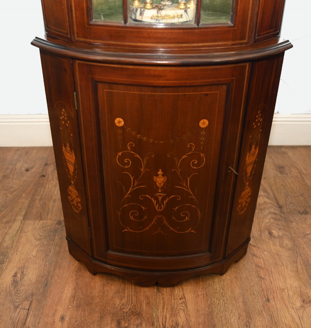 An Edwardian inlaid mahogany corner display cabinet featuring a swan-neck pediment, astragal glazed upper door, and marquetry urn designs on the lower panel. View III